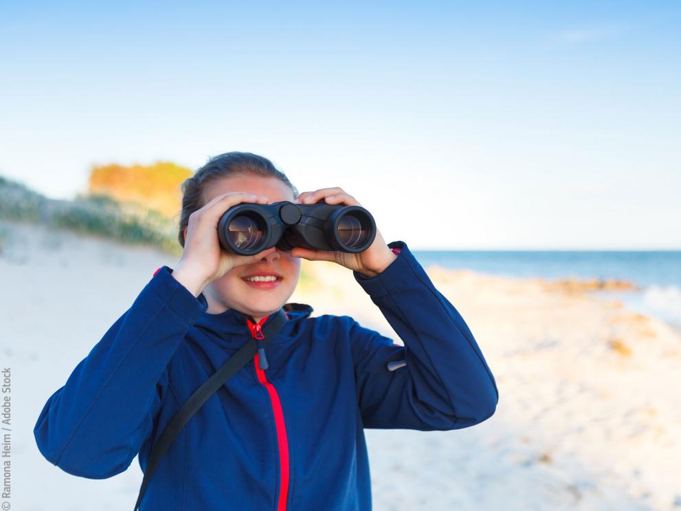 Girl looking at the sea with binoculars © Ramona Heim / Adobe Stock